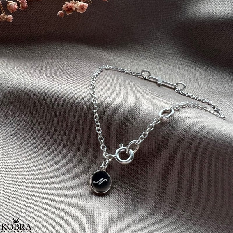 "Trust" kors armbnd i slv med lille graveret amulet