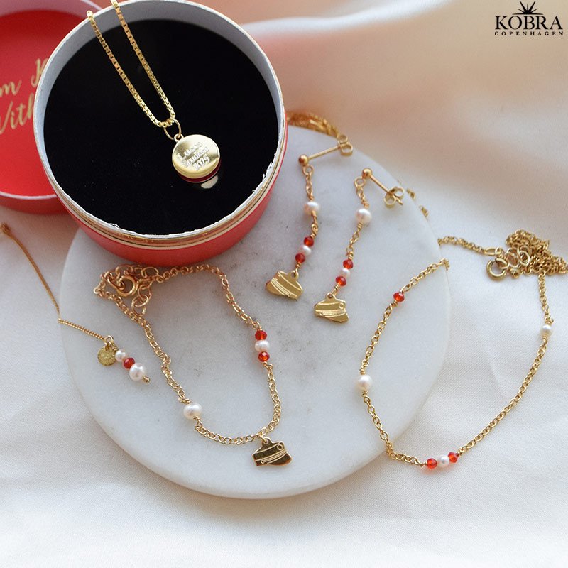 Studenter armbnd i guld med hue-vedhng og rde perler